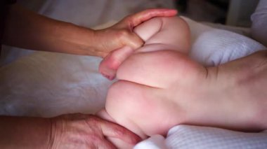 Bebek karnının üstünde yatarken bir yetişkin onlara masaj yapıyor ve hareket egzersizleri yapıyor.