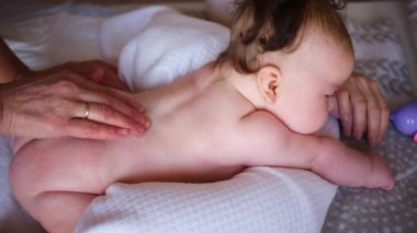 Bebek karnının üstünde yatarken bir yetişkin onlara masaj yapıyor ve hareket egzersizleri yapıyor.