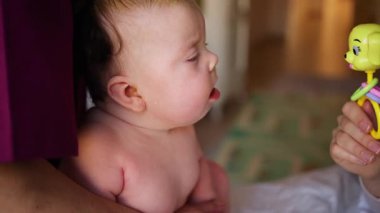 Masaj sırasında oyuncak ile battaniyeye uzanmış ağlayan bir bebeğin dikkatini dağıtmaya çalışan bir kadın.