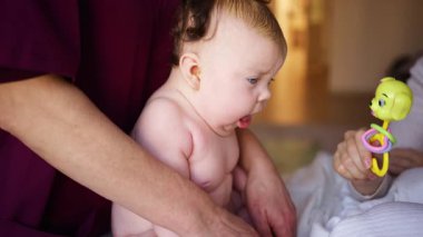 Bakıcı bebekle hareket egzersizi yapıyor. Oyuncak dikkatini dağıtıyor.