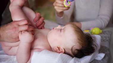 Bebek sırt üstü yatarken bir yetişkin onlara masaj yapıyor ve hareket egzersizleri yapıyor.