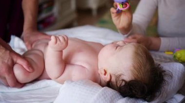 Masaj sırasında oyuncak ile battaniyeye uzanmış ağlayan bir bebeğin dikkatini dağıtmaya çalışan bir kadın.