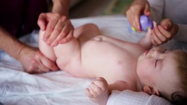 Masaj sırasında oyuncak ile battaniyeye uzanmış ağlayan bir bebeğin dikkatini dağıtmaya çalışan bir kadın.