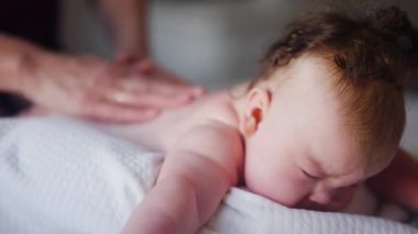 Bebek karnının üstünde yatarken bir yetişkin onlara masaj yapıyor ve hareket egzersizleri yapıyor.