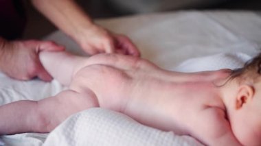 Bebek karnının üstünde yatarken bir yetişkin onlara masaj yapıyor ve hareket egzersizleri yapıyor.