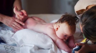 Bebek karnının üstünde yatarken bir yetişkin onlara masaj yapıyor ve hareket egzersizleri yapıyor.