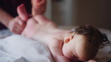 Bebek karnının üstünde yatarken bir yetişkin onlara masaj yapıyor ve hareket egzersizleri yapıyor.