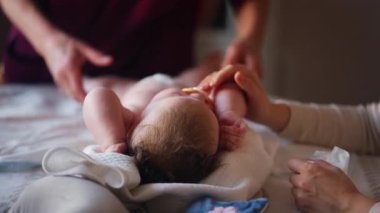 Bebek sırt üstü yatarken bir yetişkin onlara masaj yapıyor ve hareket egzersizleri yapıyor.