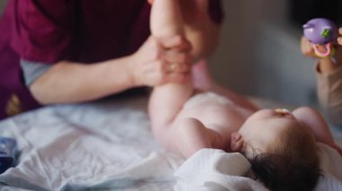 Bebek sırt üstü yatarken bir yetişkin onlara masaj yapıyor ve hareket egzersizleri yapıyor.