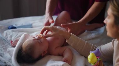 Masaj sırasında oyuncak ile battaniyeye uzanmış ağlayan bir bebeğin dikkatini dağıtmaya çalışan bir kadın.