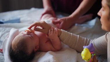 Bir oyuncak ve emzik ile masaj sırasında battaniyenin üzerinde ağlayan bir bebeğin dikkatini dağıtmaya çalışan bir kadın.