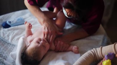 Masaj sırasında oyuncak ile battaniyeye uzanmış ağlayan bir bebeğin dikkatini dağıtmaya çalışan bir kadın.