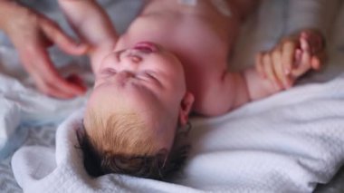 Bebek sırt üstü yatarken bir yetişkin onlara masaj yapıyor ve anne nazikçe bebeğin elini tutuyor.