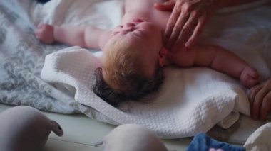 Bebek sırt üstü yatarken bir yetişkin onlara masaj yapıyor ve anne nazikçe bebeğin elini tutuyor.