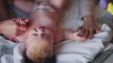 Bebek sırt üstü yatarken bir yetişkin onlara masaj yapıyor ve anne nazikçe bebeğin elini tutuyor.