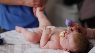 Bebek emzik ile sırt üstü yatarken yetişkinler nazik kol ve bacak hareketlerinde yardımcı oluyorlar.