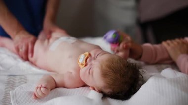 Bebek emzik ile sırt üstü yatarken yetişkinler nazik kol ve bacak hareketlerinde yardımcı oluyorlar.