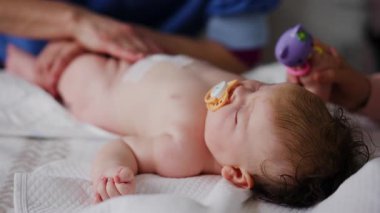 Bebek emzik ile sırt üstü yatarken yetişkinler nazik kol ve bacak hareketlerinde yardımcı oluyorlar.