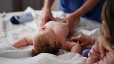 Bebek sırt üstü yatarken bir yetişkin onlara masaj yapıyor ve anne nazikçe bebeğin elini tutuyor.