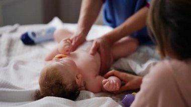 Bebek sırt üstü yatarken bir yetişkin onlara masaj yapıyor ve anne nazikçe bebeğin elini tutuyor.