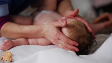 Bebek sırt üstü yatarken bir yetişkin onlara masaj yapıyor ve hareket egzersizleri yapıyor.