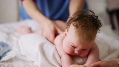 Bebek karnının üstünde yatarken bir yetişkin onlara masaj yapıyor ve hareket egzersizleri yapıyor.
