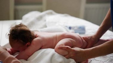Bebek karnının üstünde yatarken bir yetişkin onlara masaj yapıyor ve hareket egzersizleri yapıyor.