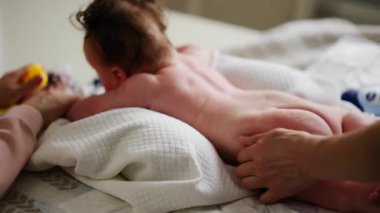 Bebek karnının üstünde yatarken bir yetişkin onlara masaj yapıyor ve hareket egzersizleri yapıyor.