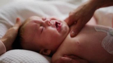 Bebek sırt üstü yatarken bir yetişkin onlara masaj yapıyor ve hareket egzersizleri yapıyor.