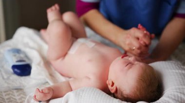 Masaj sırasında oyuncak ile battaniyeye uzanmış ağlayan bir bebeğin dikkatini dağıtmaya çalışan bir kadın.