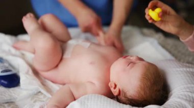 Masaj sırasında oyuncak ile battaniyeye uzanmış ağlayan bir bebeğin dikkatini dağıtmaya çalışan bir kadın.