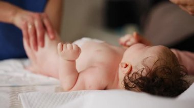 Bebek sırt üstü yatarken bir yetişkin onlara masaj yapıyor ve hareket egzersizleri yapıyor.