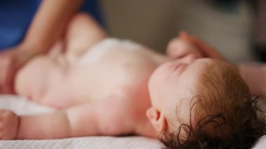 Bebek sırt üstü yatarken bir yetişkin onlara masaj yapıyor ve hareket egzersizleri yapıyor.