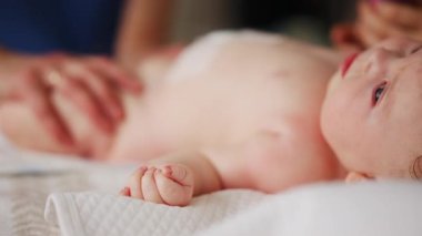 Bebek sırt üstü yatarken bir yetişkin onlara masaj yapıyor ve hareket egzersizleri yapıyor.