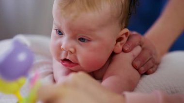 Woman trying to distract a crying baby lying on a blanket during massage with a toy