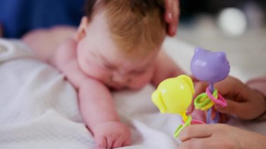 Masaj sırasında oyuncak ile battaniyeye uzanmış ağlayan bir bebeğin dikkatini dağıtmaya çalışan bir kadın.