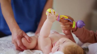 Masaj sırasında oyuncak ile battaniyeye uzanmış ağlayan bir bebeğin dikkatini dağıtmaya çalışan bir kadın.