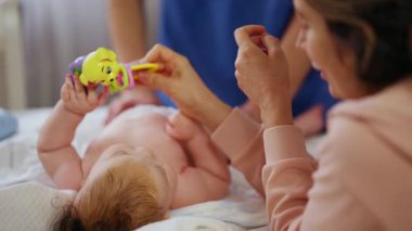 Masaj sırasında oyuncak ile battaniyeye uzanmış ağlayan bir bebeğin dikkatini dağıtmaya çalışan bir kadın.
