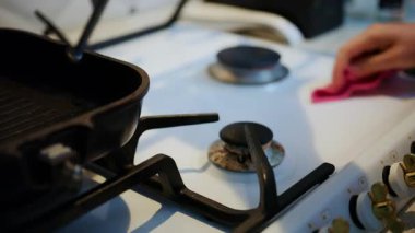 Ev içi gaz sobasını ocağa dökme demir tavayla temizleyen bir kadının yakın çekimi.