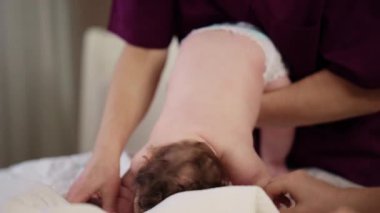 Bebek karnının üstünde yatarken bir yetişkin onlara masaj yapıyor ve hareket egzersizleri yapıyor.