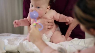 Masaj sırasında oyuncak ile battaniyeye uzanmış ağlayan bir bebeğin dikkatini dağıtmaya çalışan bir kadın.