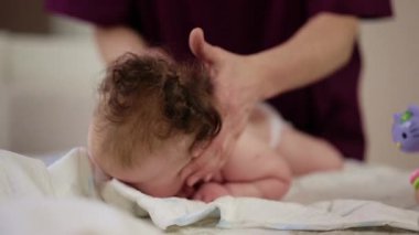 Masaj sırasında oyuncak ile battaniyeye uzanmış ağlayan bir bebeğin dikkatini dağıtmaya çalışan bir kadın.