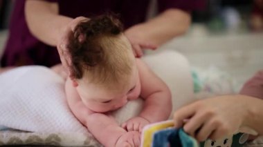 Bebek karnının üstünde yatarken bir yetişkin onlara masaj yapıyor ve hareket egzersizleri yapıyor.