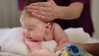 Baby lying on their tummy while an adult massages them and performs mobility exercises