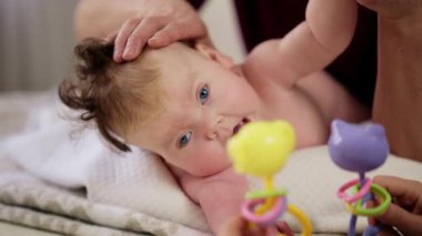 Masaj sırasında oyuncak ile battaniyeye uzanmış ağlayan bir bebeğin dikkatini dağıtmaya çalışan bir kadın.