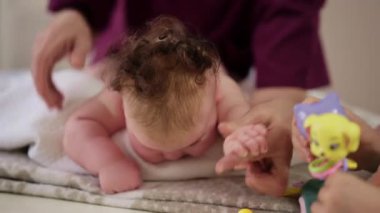 Masaj sırasında oyuncak ile battaniyeye uzanmış ağlayan bir bebeğin dikkatini dağıtmaya çalışan bir kadın.