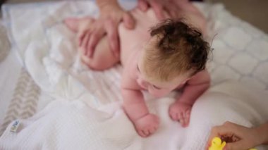 Masaj sırasında oyuncak ile battaniyeye uzanmış ağlayan bir bebeğin dikkatini dağıtmaya çalışan bir kadın.