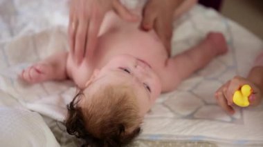 Masaj sırasında oyuncak ile battaniyeye uzanmış ağlayan bir bebeğin dikkatini dağıtmaya çalışan bir kadın.