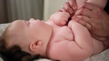 Bebek sırt üstü yatarken bir yetişkin onlara masaj yapıyor ve hareket egzersizleri yapıyor.