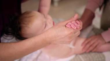 Bebek sırt üstü yatarken bir yetişkin onlara masaj yapıyor ve hareket egzersizleri yapıyor.